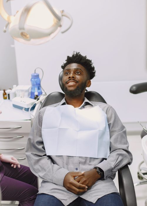 Young african-american man. Guy visiting dentist's office for prevention of the oral cavity. Man and famale doctor while checkup teeth.